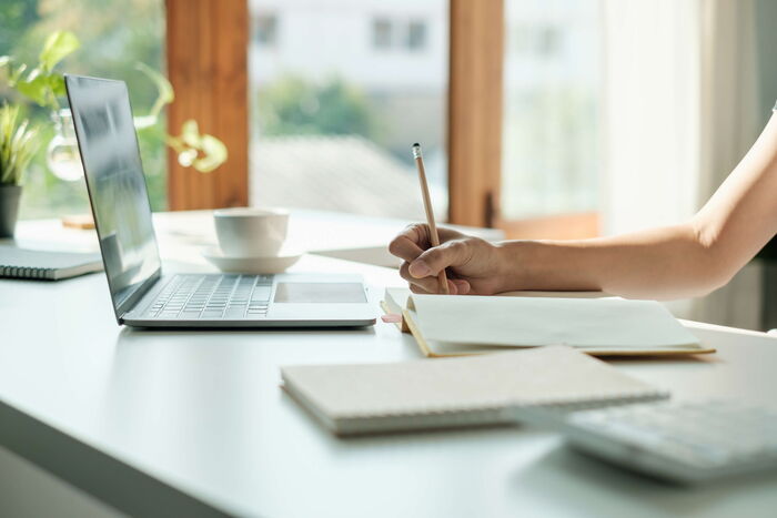 Blick auf einen Schreibtisch mit Laptop und Notitzbuch